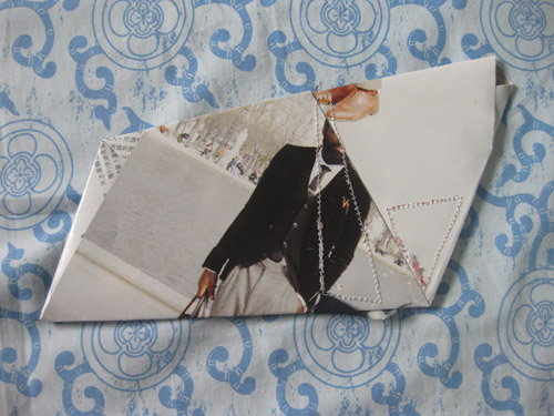 A figure in black cut against wide white planes, beaded thread running along the folded edge