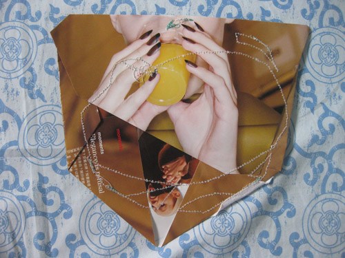 Two hands cupping a yellow fruit on a gold ground, beaded stitching looping across the fold