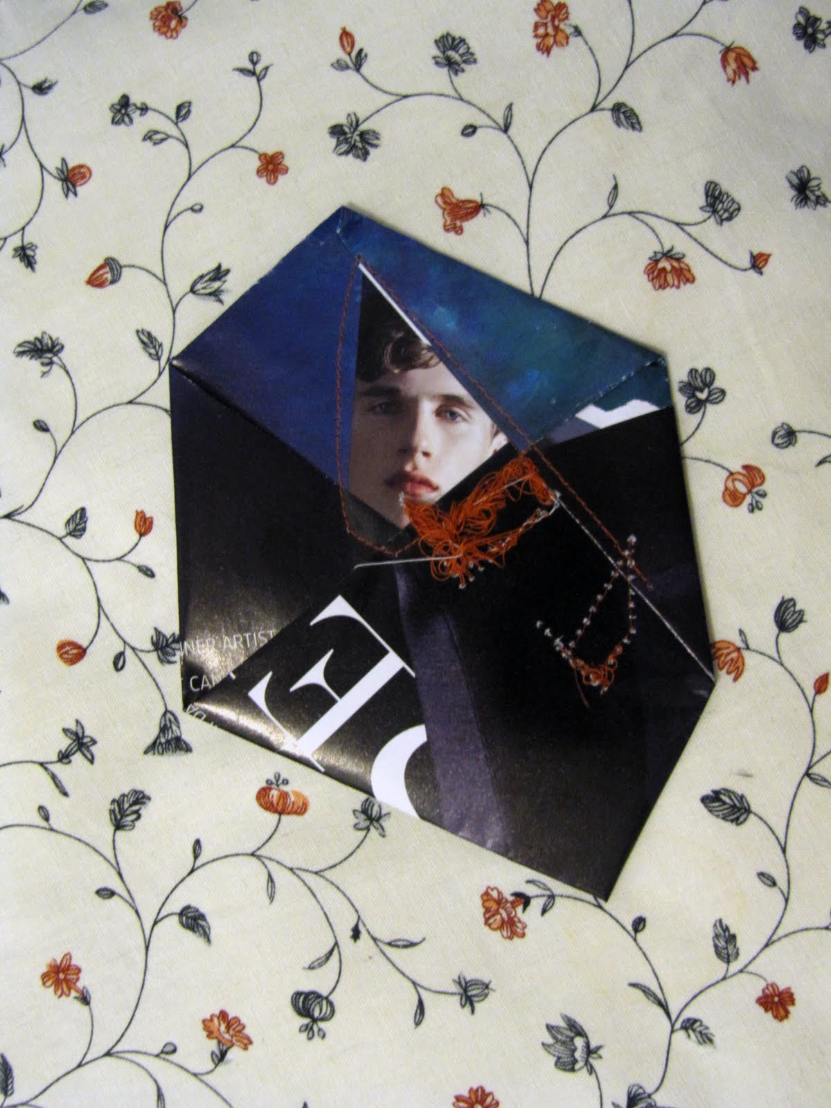 A young man's face on deep blue, a cut letter beside him, orange thread knotted through the fold