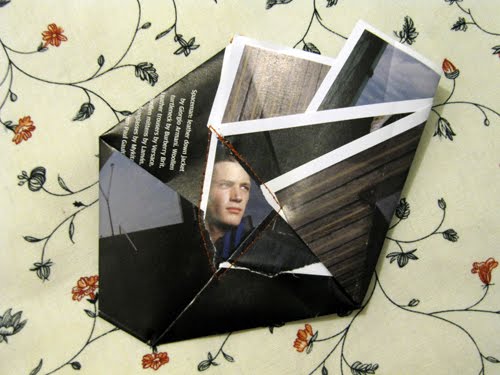 White zigzag strips cut across a man's face in a dark folded envelope, stitched at one corner