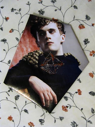 A young man in a gold studded collar against red, a beaded necklace stitched over his chest